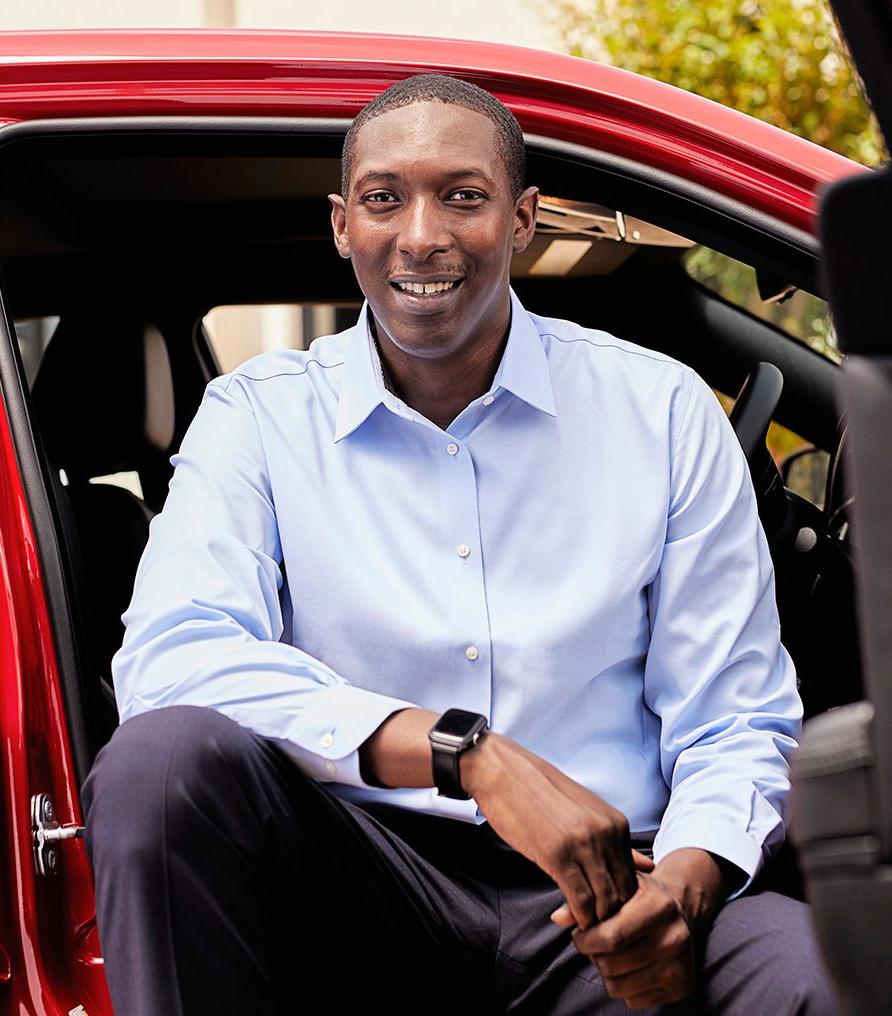 Dark-skinned gentleman with a light blue shirt sitting in a red vehicle and smiling.